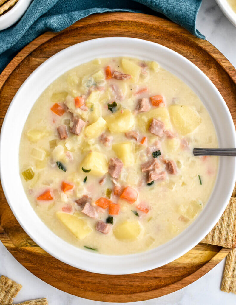 Closeup of a bowl of Slow Cooker Ham and Potato Soup on a wooden platter served with triscuit crackers.