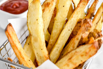 Air Fried French Fries in a silver serving basket set on a table next to a small bowl of ketchup.