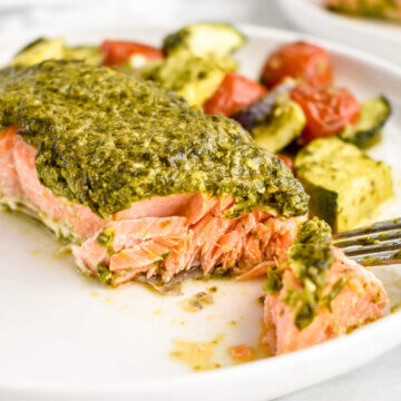 Baked Pesto Salmon with roasted zucchini, cherry tomatoes and onions on a plate.