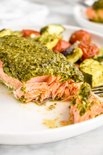 Baked Pesto Salmon with roasted zucchini, cherry tomatoes and onions on a plate.