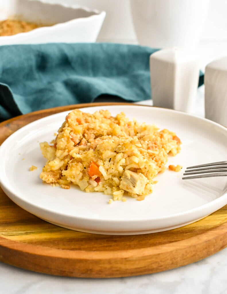 A portion of creamy chicken and rice casserole on a white dinner plate set on a wooden charger plate on a table next to a teal napkin.