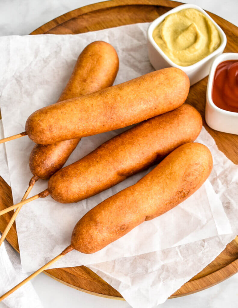 Golden brown corn dogs set on a parchment lined wooden platter.