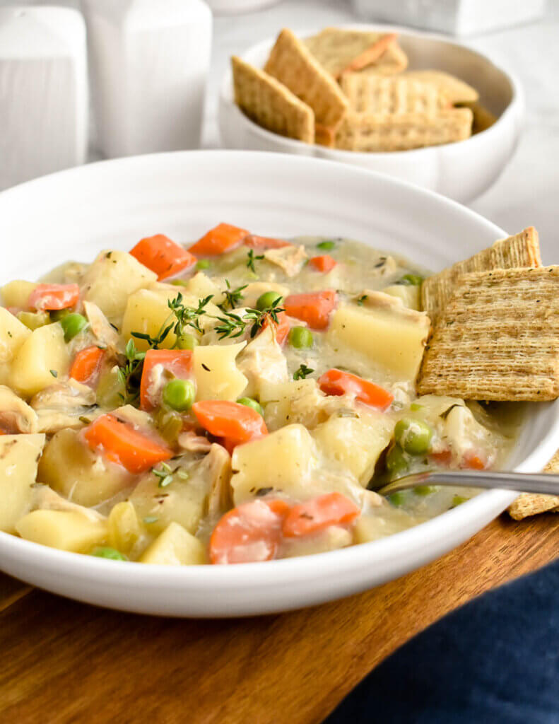 A bowl of creamy chicken stew served alongside crackers.