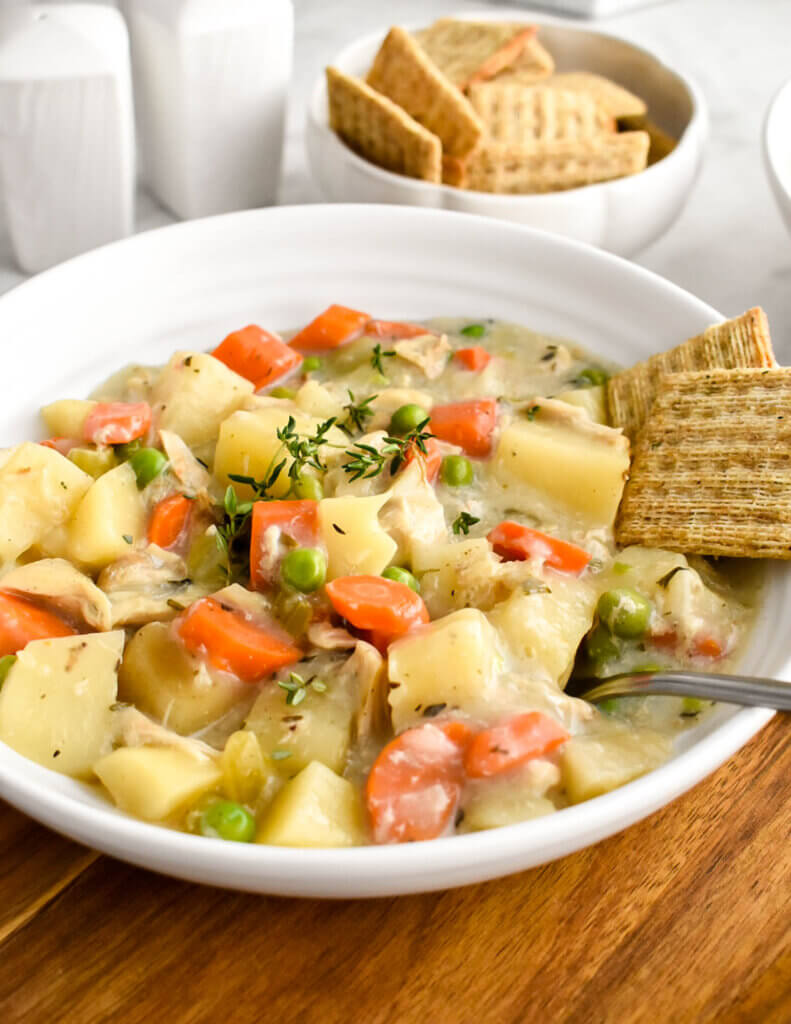 Closeup of a bowl of creamy chicken stew served with crackers.