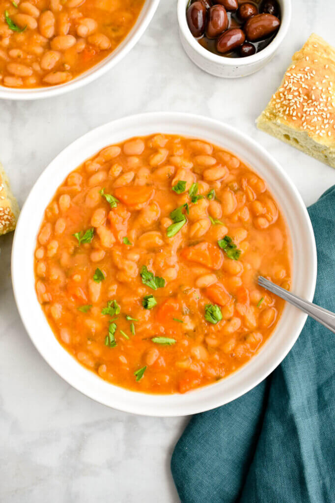 A bowl of Greek bean soup topped with parsley and served with olives and bread.