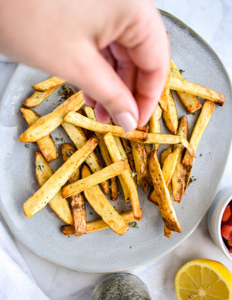 A platter of french fries being sprinkled with dried oregano.