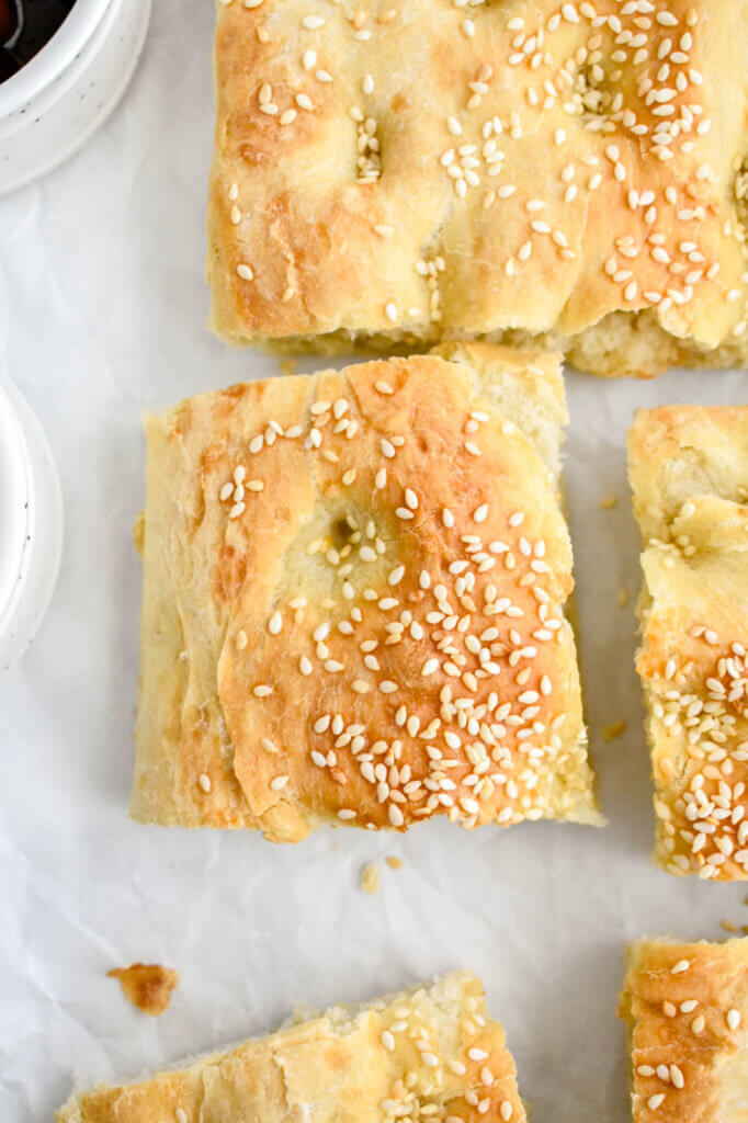 Closeup of a square slice of lagana bread sprinkled with sesame seeds.