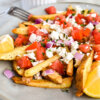 Closeup of a platter of french fries topped with diced tomato, onion, and crumbled feta.