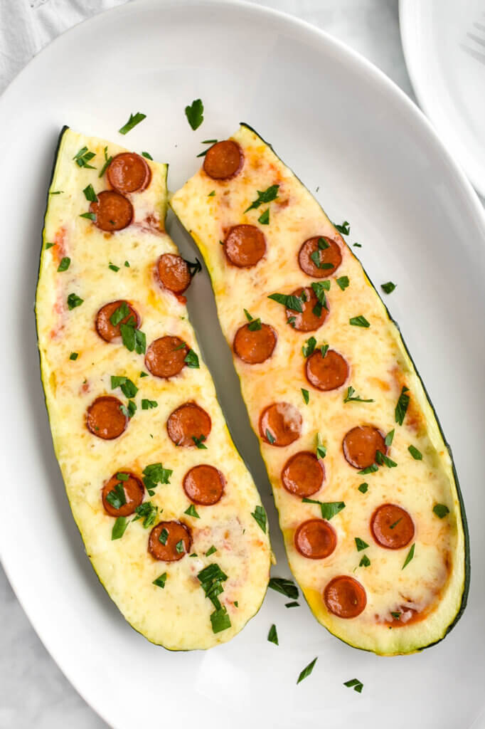 Low Carb Pizza Stuffed Zucchini Boats topped with pepperoni and parsley and served on an oval platter.