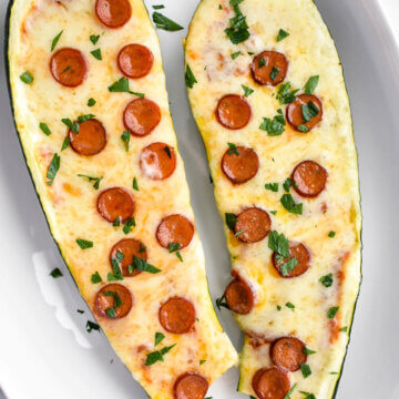 Two pizza stuffed zucchini boats topped with mini pepperoni served in an oval platter.