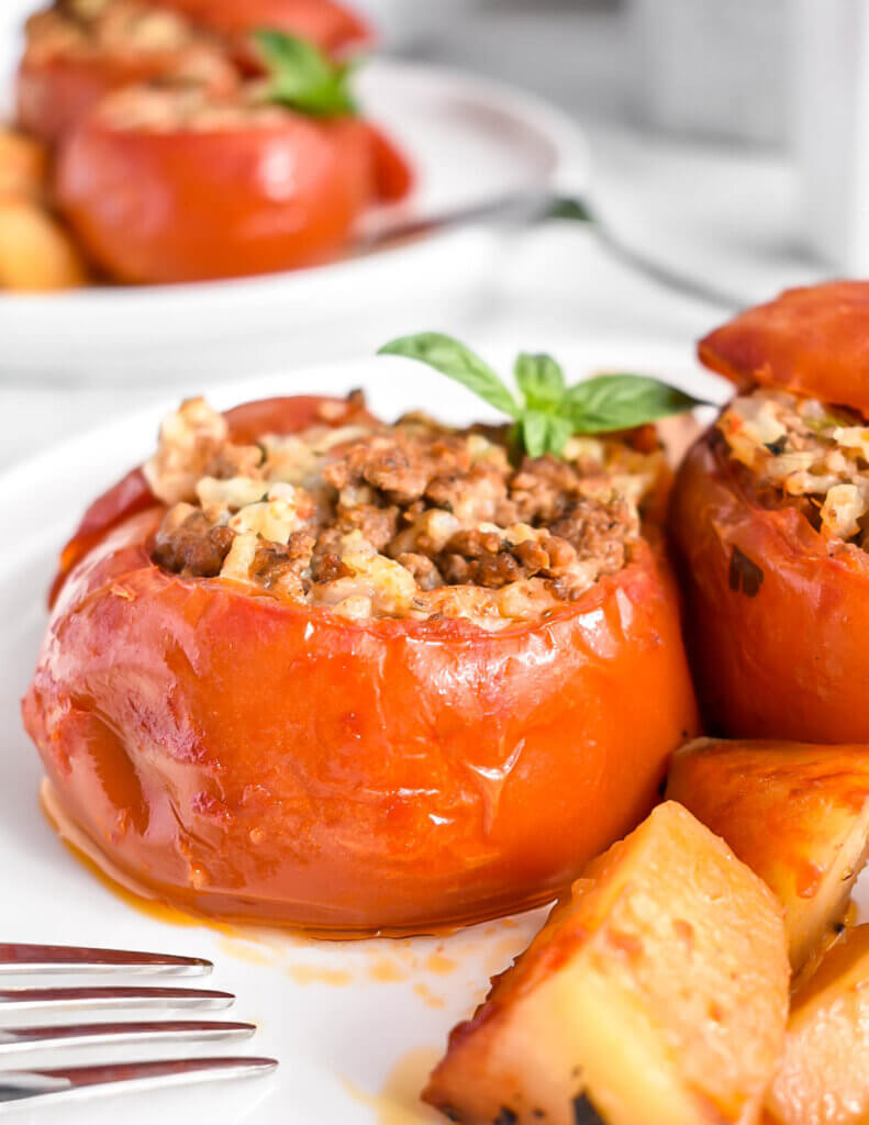 Closeup of stuffed tomato with rice and beef on a plate with potatoes.