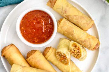 A platter of crispy vegetable spring rolls served with sweet chili sauce.