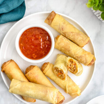 A platter of crispy vegetable spring rolls served with sweet chili sauce.