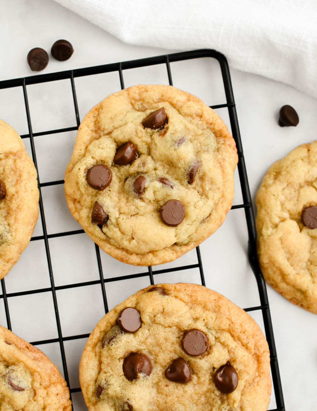 Closeup of a chewy chocolate chip cookie on a black cooling rack.
