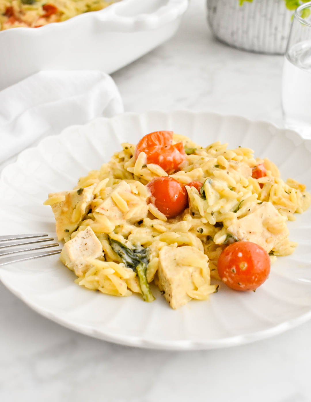 Boursin chicken orzo bake on a white scalloped plate set on a grey marble counter.