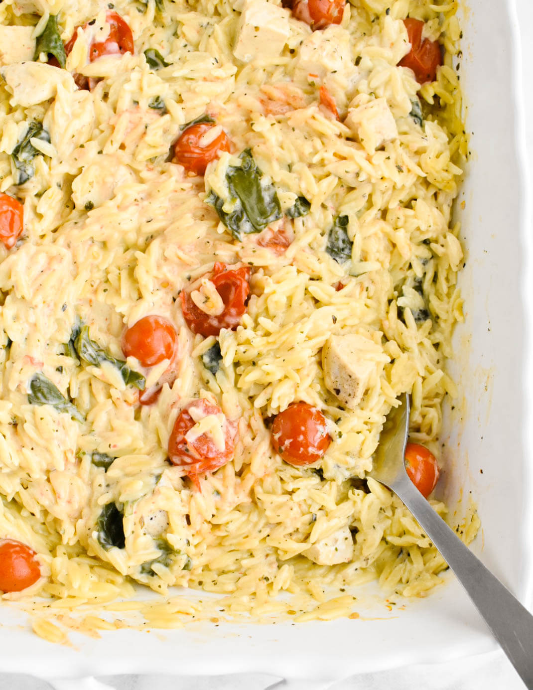 Boursin orzo bake studded with cherry tomatoes, spinach, and chicken pieces in a baking dish.