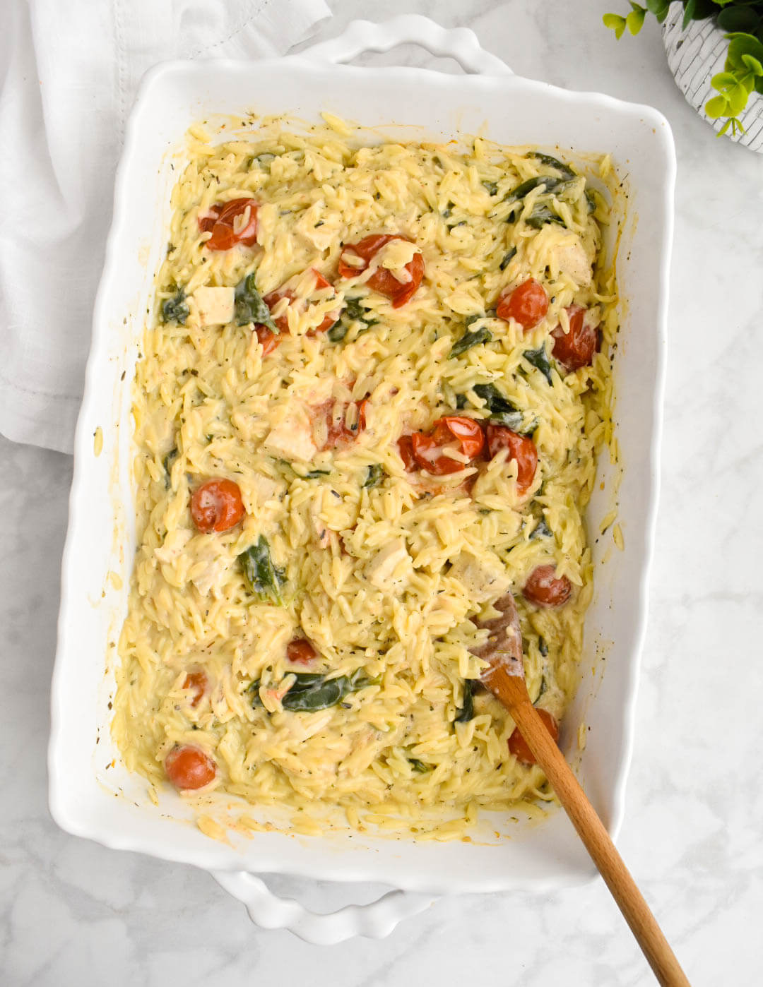 A white baking dish containing chicken, cherry tomatoes, spinach, and orzo covered in a creamy boursin sauce.