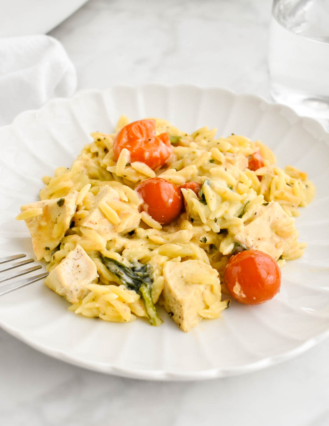 Boursin chicken orzo bake on a white scalloped plate set on a grey marble counter.