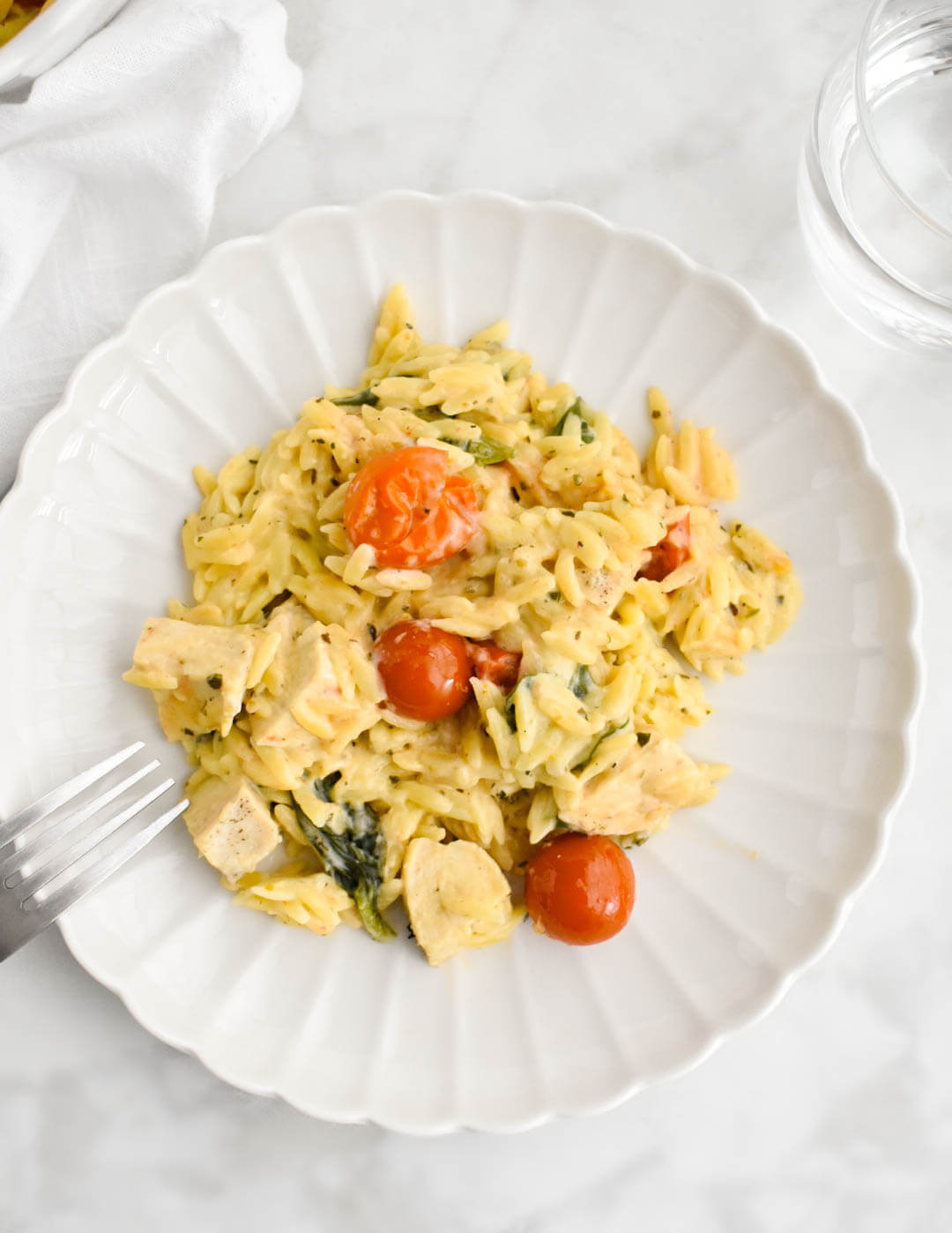 Boursin chicken orzo bake on a white scalloped plate set on a grey marble counter.