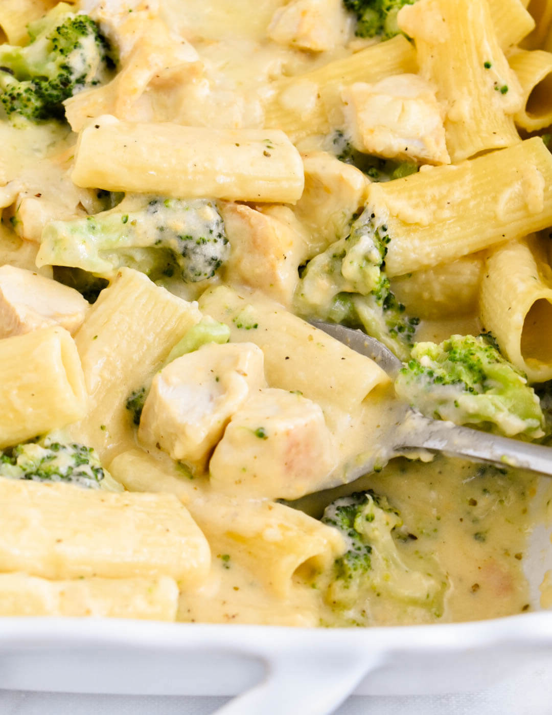Closeup of chicken and broccoli pasta bake being scooped from a baking pan.