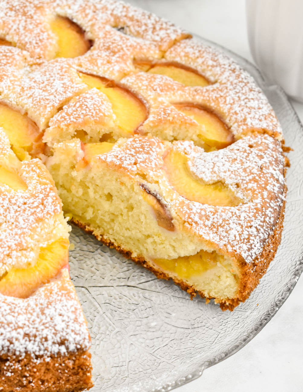 Closeup of a sliced peach cake showing the tender crumb studded with peach slices.