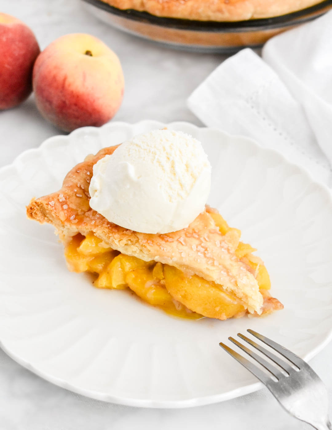 A slice of peach pie topped with a scoop of vanilla ice cream.