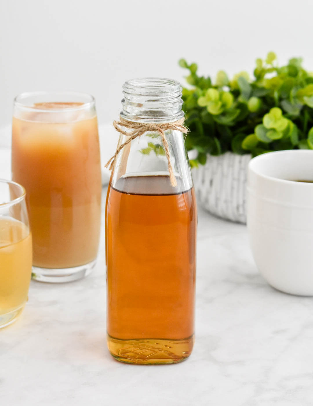 Closeup of bottled vanilla simple syrup set next to an iced coffee, hot coffee, and cocktail.