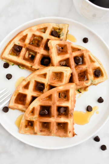 A zucchini waffle cut into quarters and topped with chocolate chips and maple syrup.