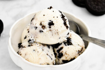 A bowl of simple Oreo ice cream set on a grey marble counter next to Oreo cookies.