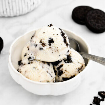 A bowl of simple Oreo ice cream set on a grey marble counter next to Oreo cookies.