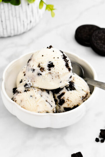 A bowl of simple Oreo ice cream set on a grey marble counter next to Oreo cookies.