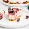 A plated slice of cranberry cheesecake showing swirls of cranberry sauce and topped with sugared cranberries.