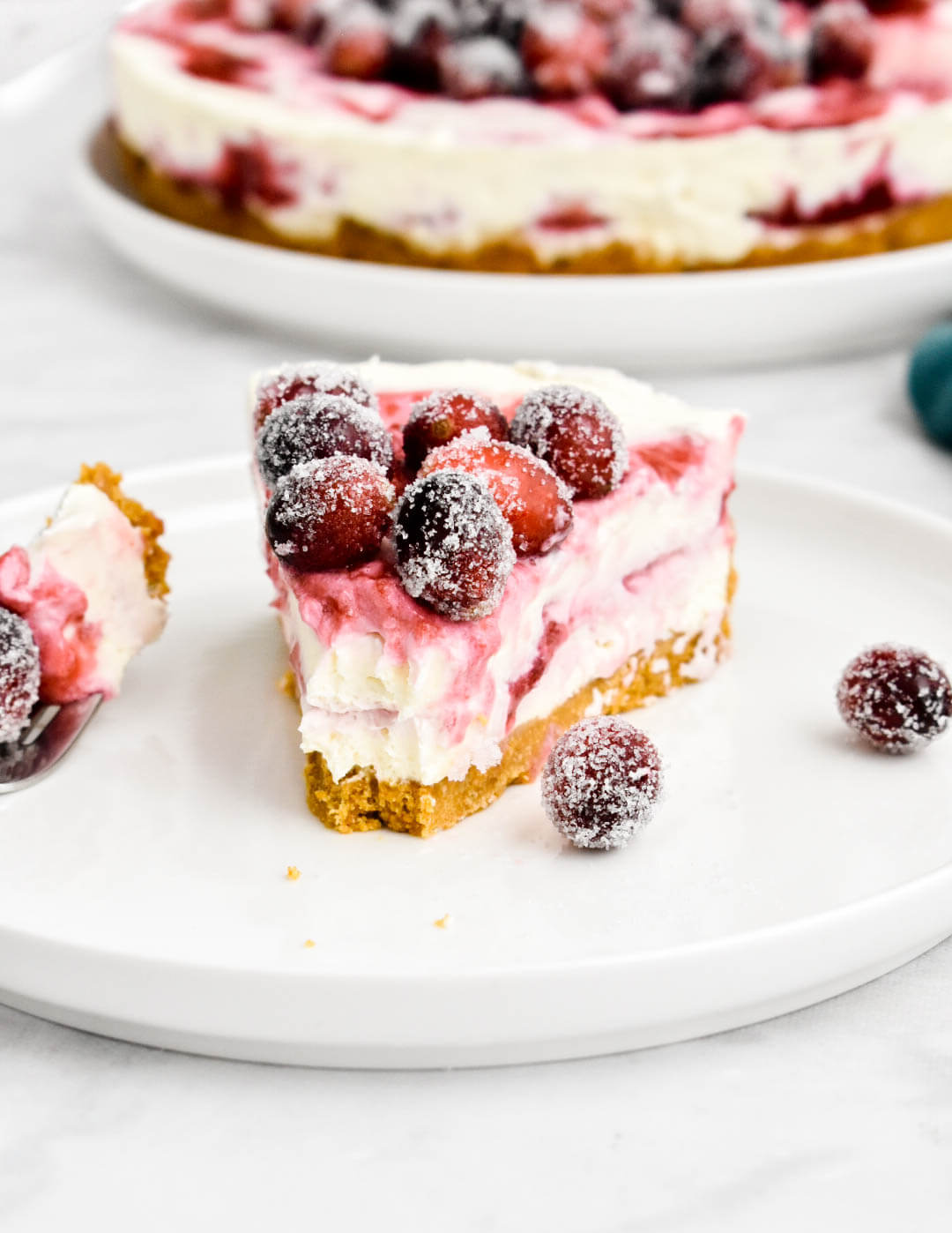 A plated slice of cranberry cheesecake showing swirls of cranberry sauce and topped with sugared cranberries.