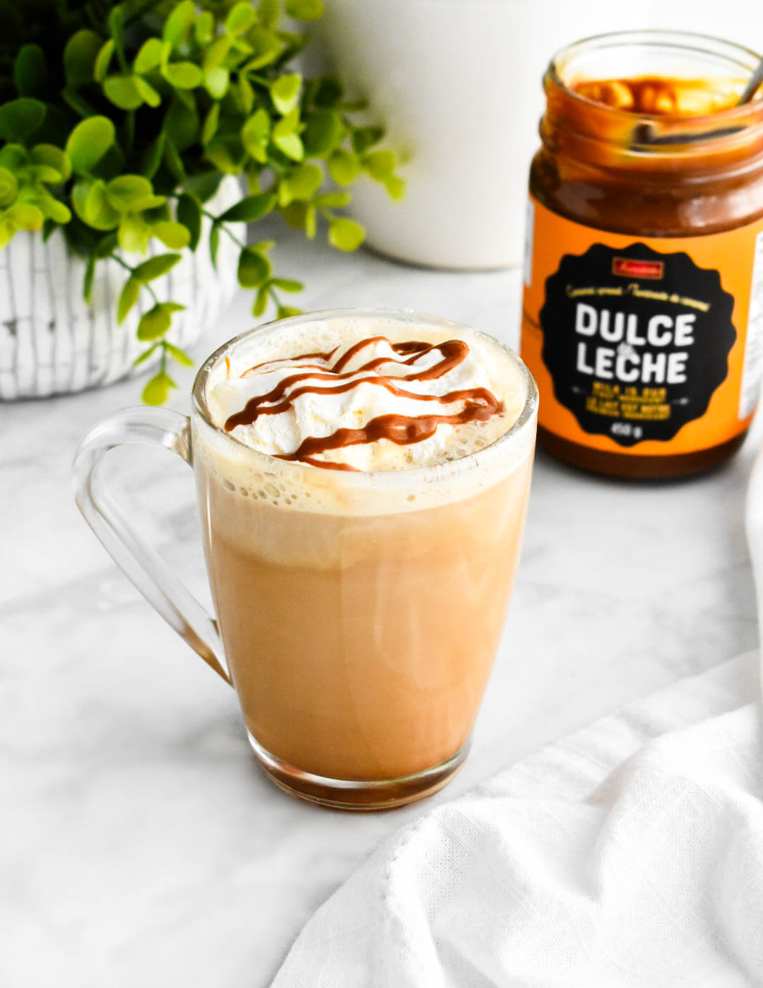 A clear mug of dulce de leche latte next to a jar of dulce de leche.