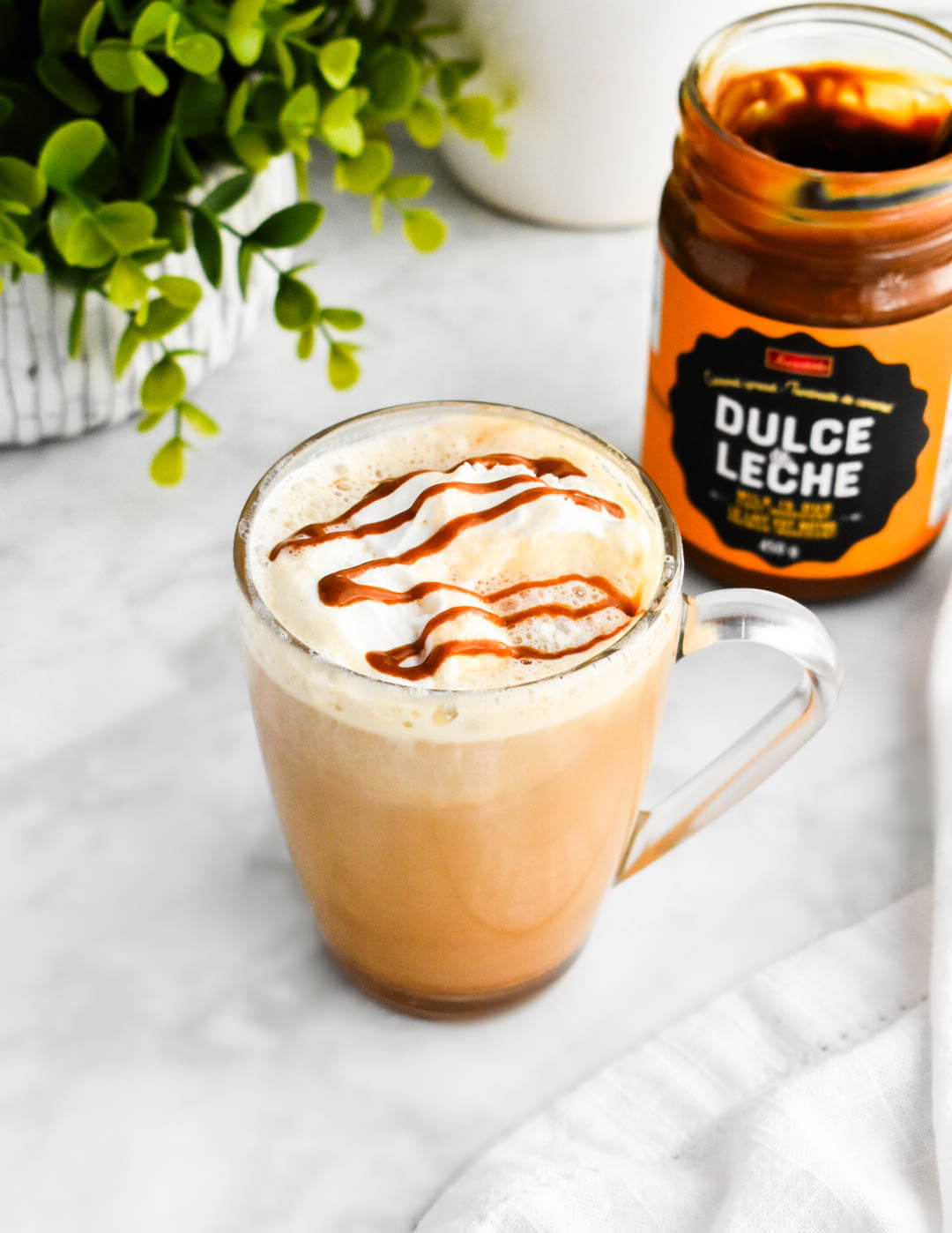 A clear mug of dulce de leche latte next to a jar of dulce de leche.