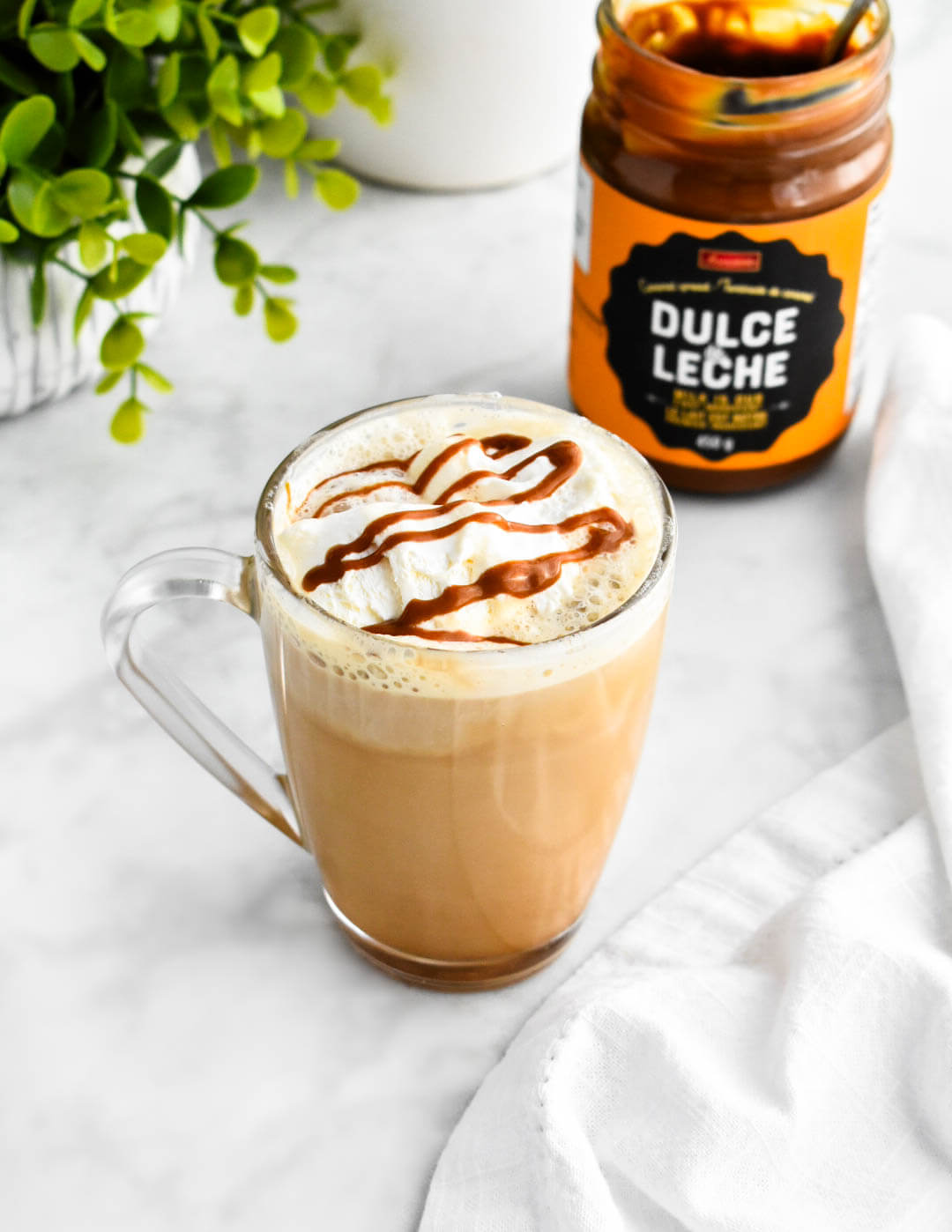 A clear mug of dulce de leche latte next to a jar of dulce de leche.