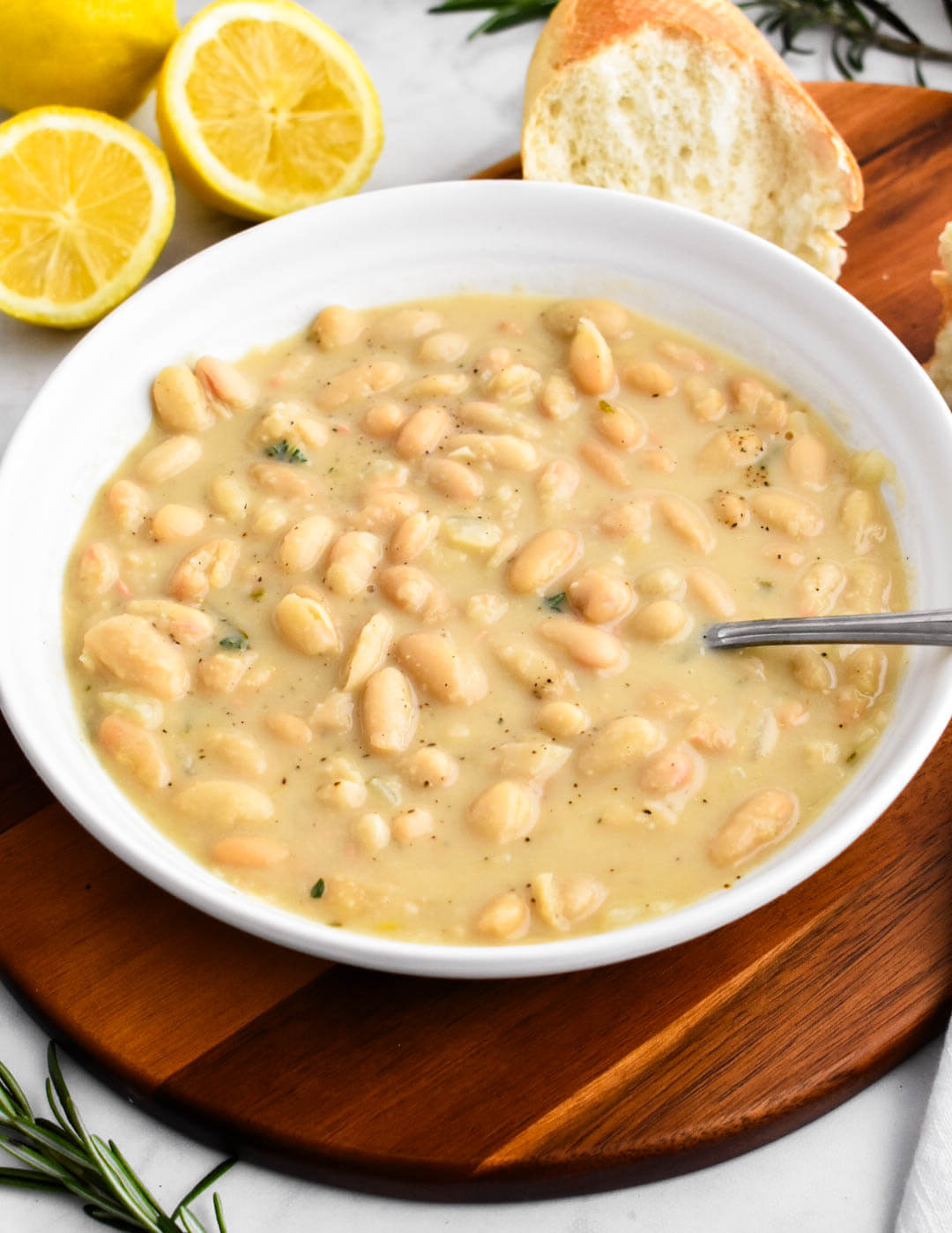 A bowl of creamy white bean soup served with sliced lemon and bread.