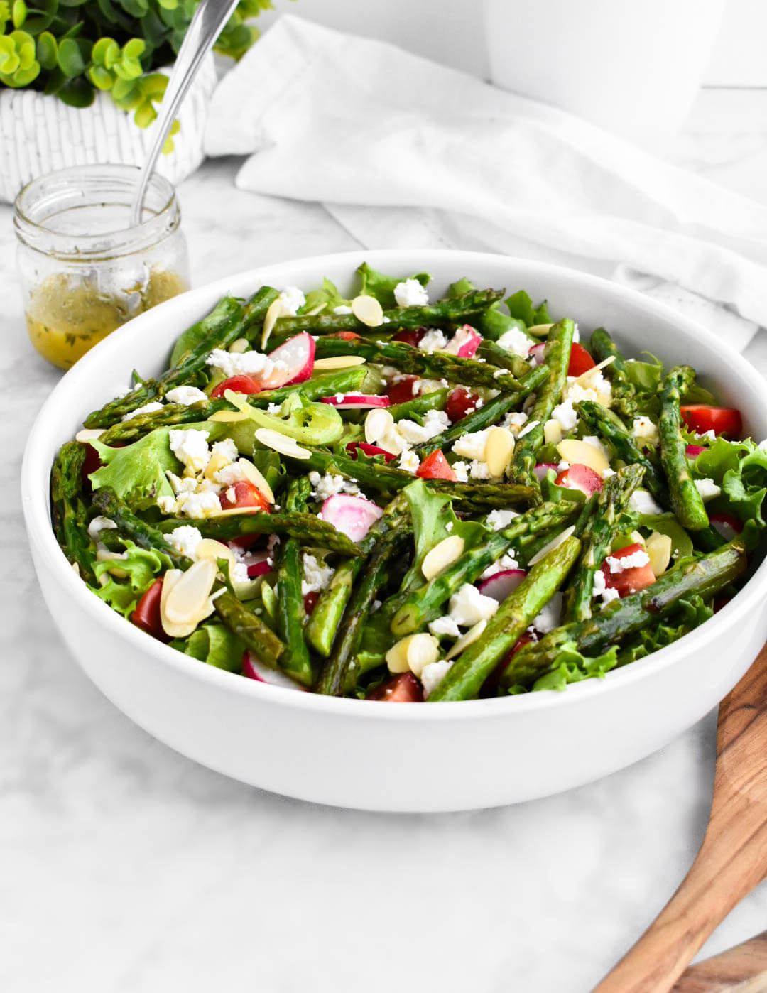 A bowl of asparagus salad with radishes, tomatoes, feta and almond slices.