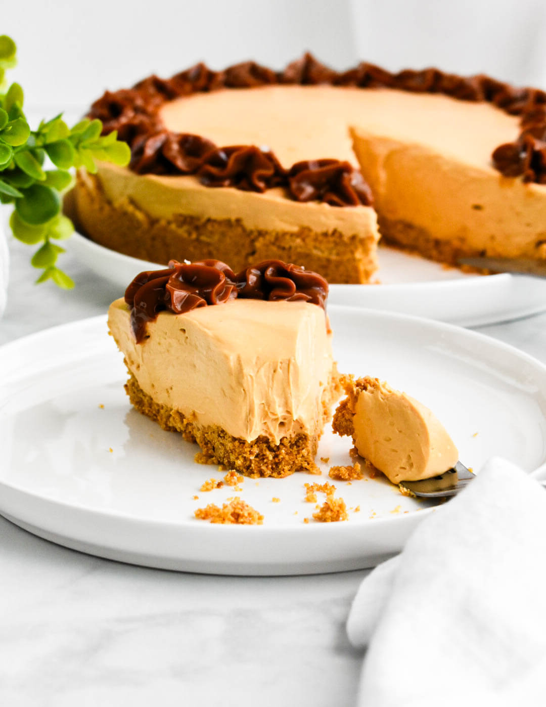 A plated slice of dulce de leche cheesecake set down next to the remaining cheesecake.