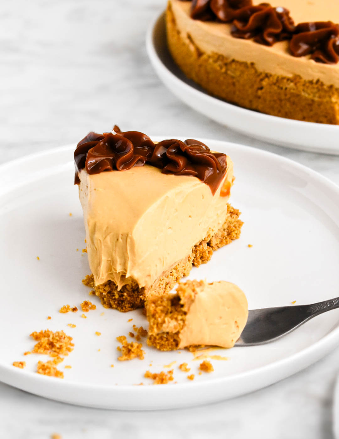 A slice of dulce de leche cheesecake with a forkful of cheesecake broken away.