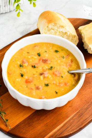 A bowl of slow cooker split pea soup sprinkled with fresh thyme and set next to crusty bread.