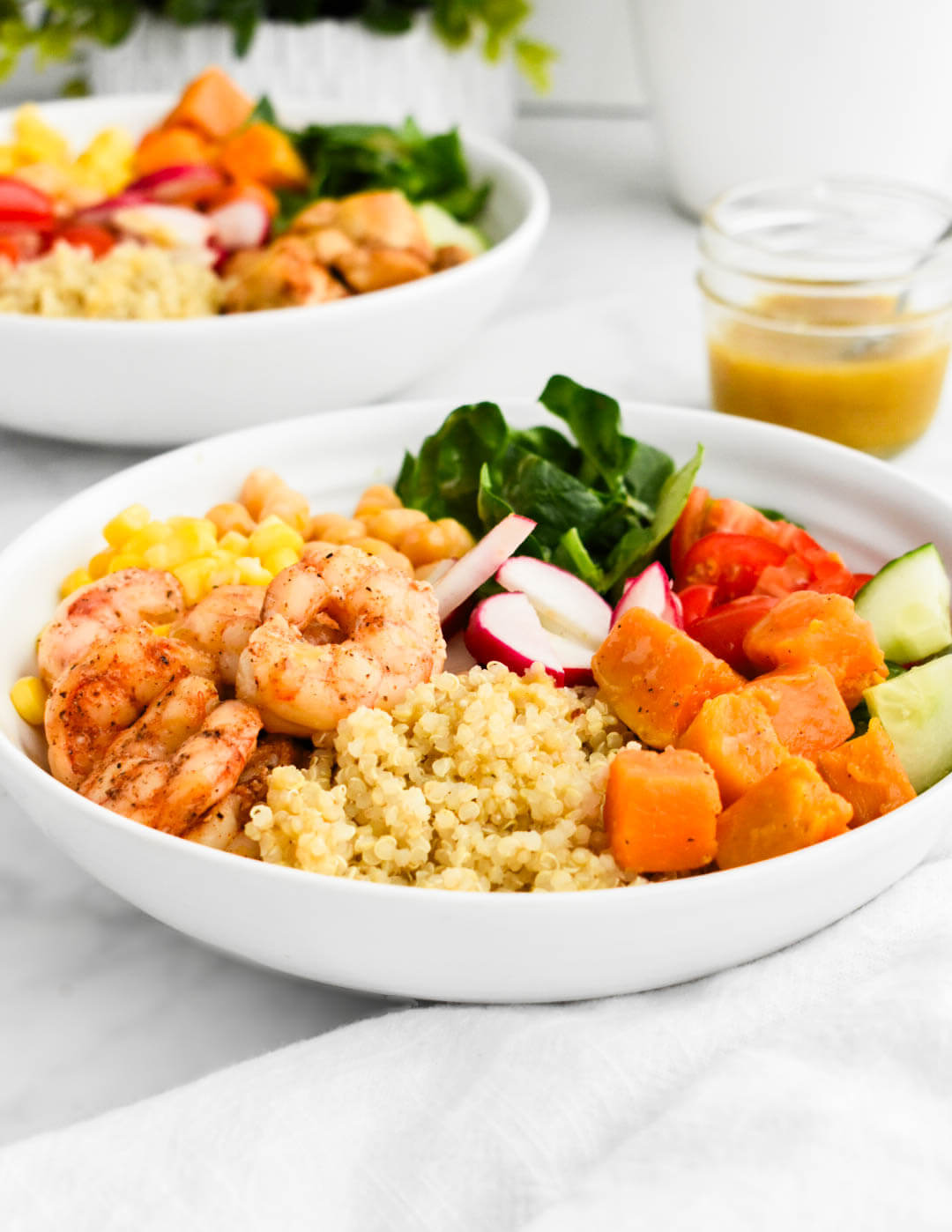 Closeup of a power bowl made with quinoa, shrimp, spinach, cucumbers, tomatoes, corn, sweet potatoes, chickpeas and radishes.