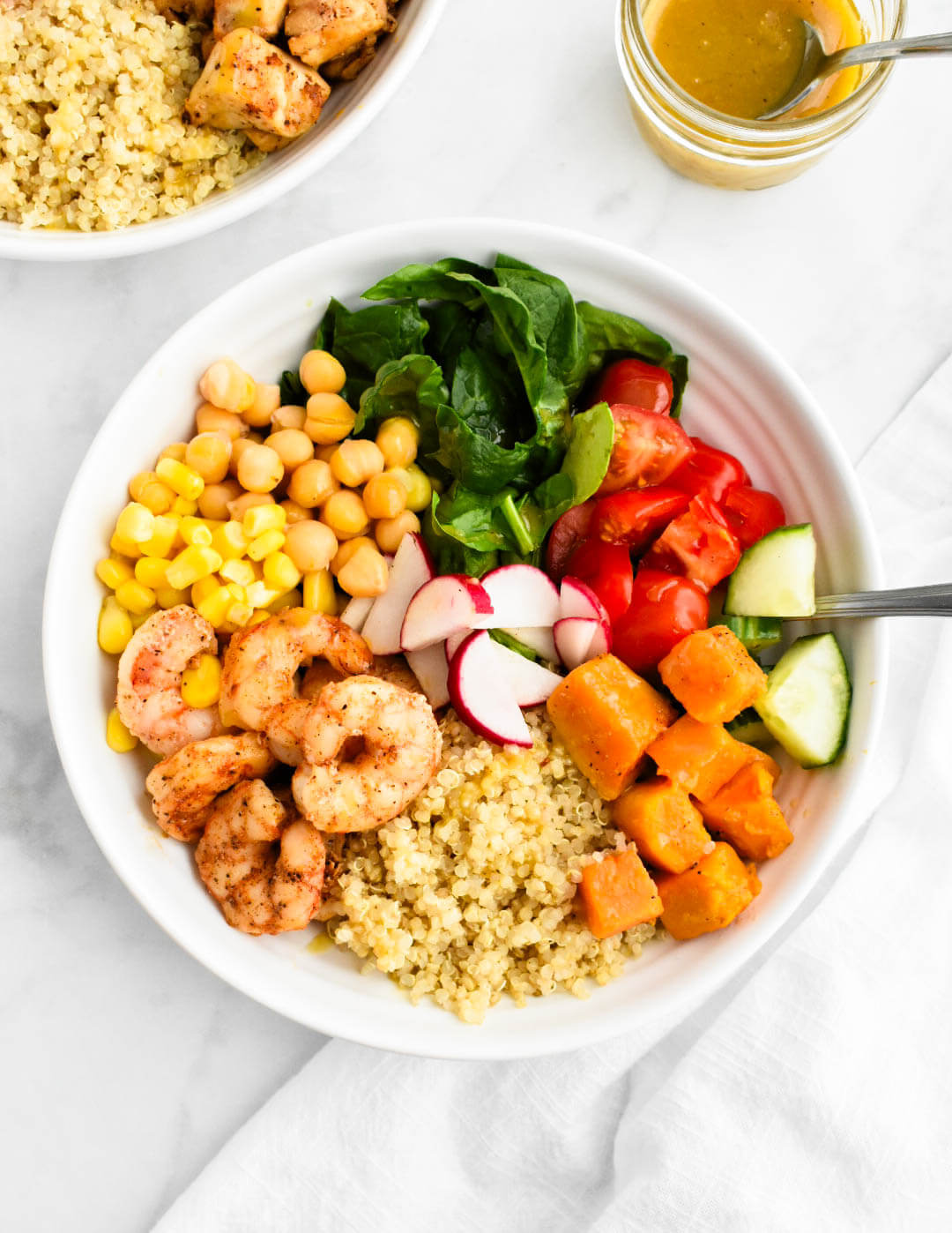 A power bowl made with quinoa, shrimp, spinach, cucumbers, tomatoes, corn, sweet potatoes, chickpeas and radishes.