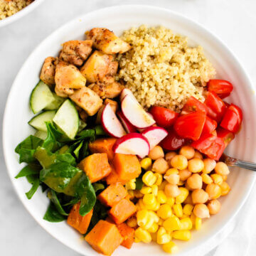 A power bowl made with quinoa, chicken, spinach, cucumbers, tomatoes, corn, sweet potatoes, chickpeas and radishes.