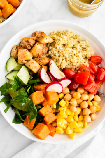 A power bowl made with quinoa, chicken, spinach, cucumbers, tomatoes, corn, sweet potatoes, chickpeas and radishes.