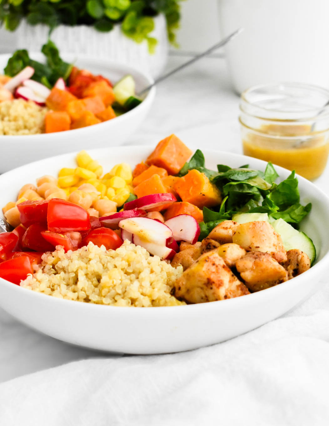 Closeup of a power bowl made with quinoa, chicken, spinach, cucumbers, tomatoes, corn, sweet potatoes, chickpeas and radishes.