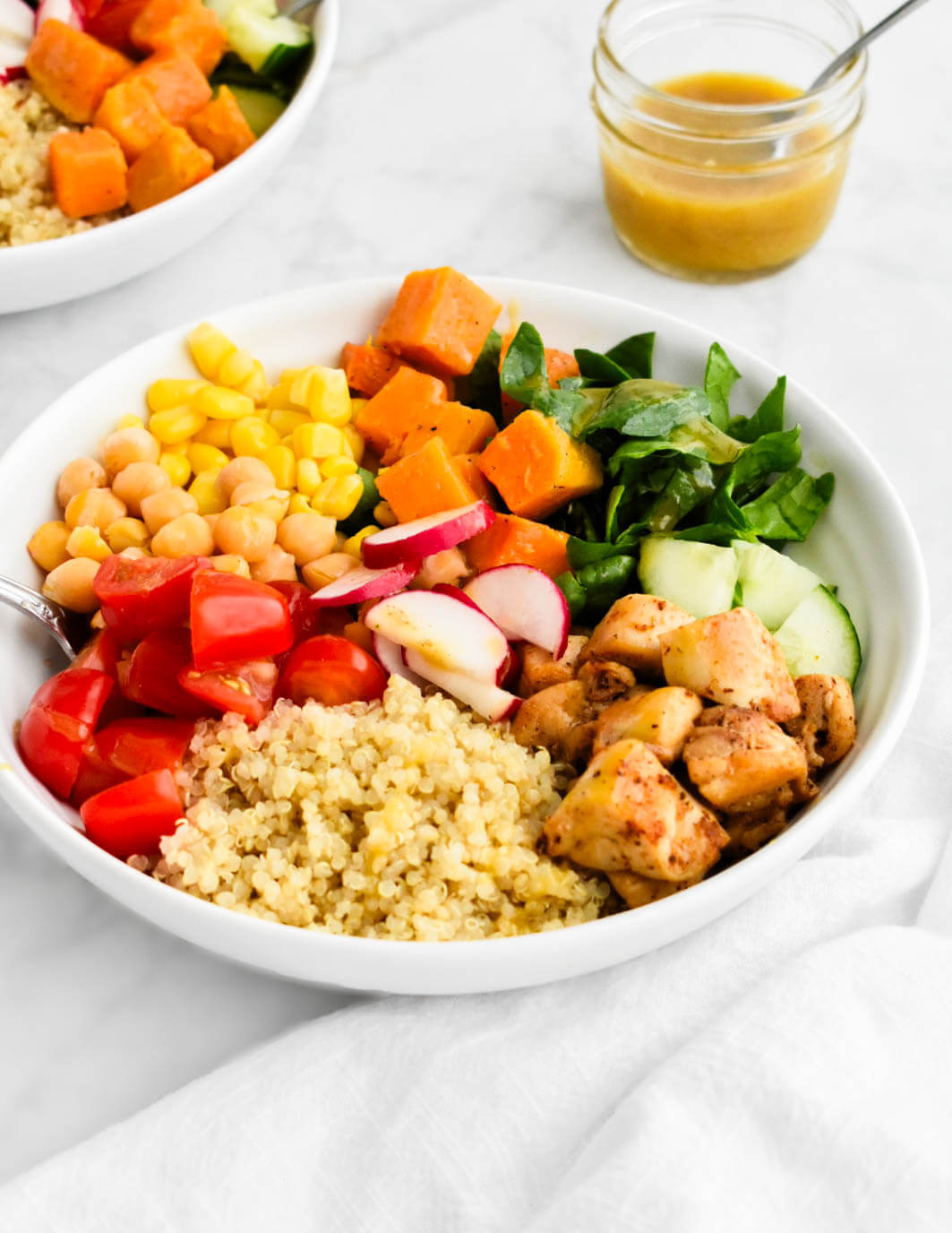 A power bowl made with quinoa, chicken, spinach, cucumbers, tomatoes, corn, sweet potatoes, chickpeas and radishes.
